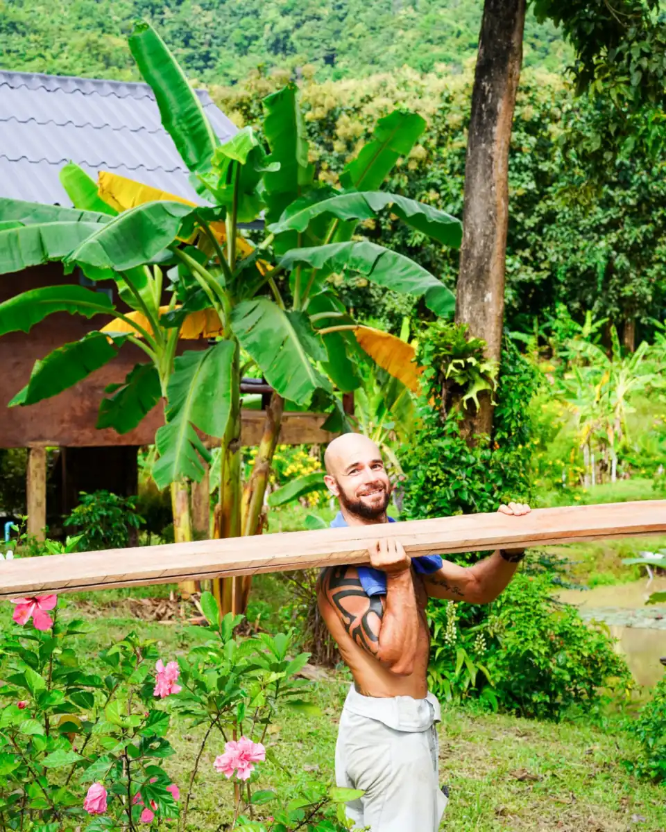 Adam carrying a long bamboo pole through the garden