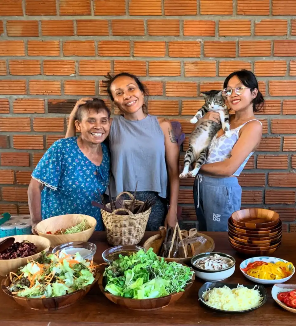 Yai, Ning and YuYe with a table of fresh dishes and a cat