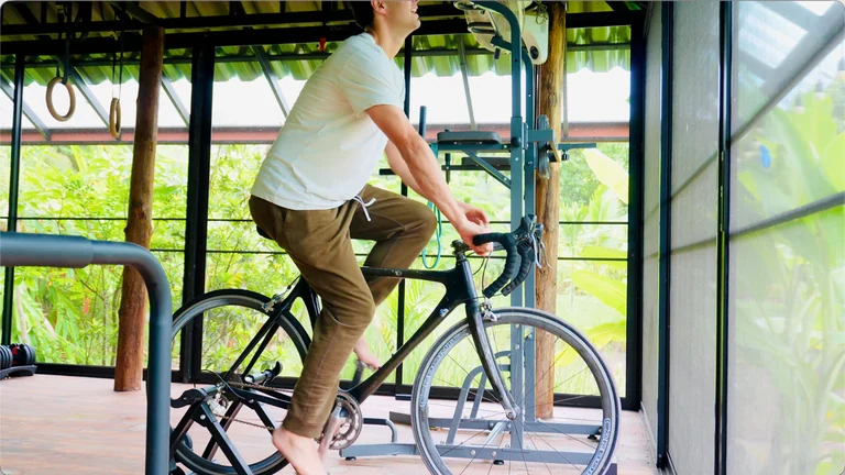 A guest cycling indoors beside open windows overlooking the banana plantation