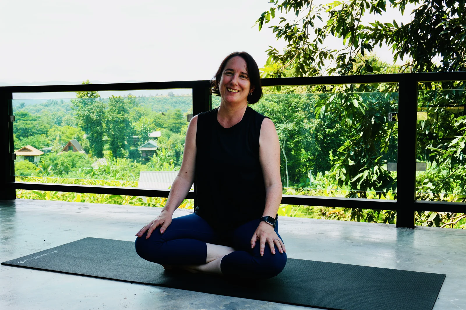 A guest sitting quietly in meditation in the open-air shala with the gardens behind