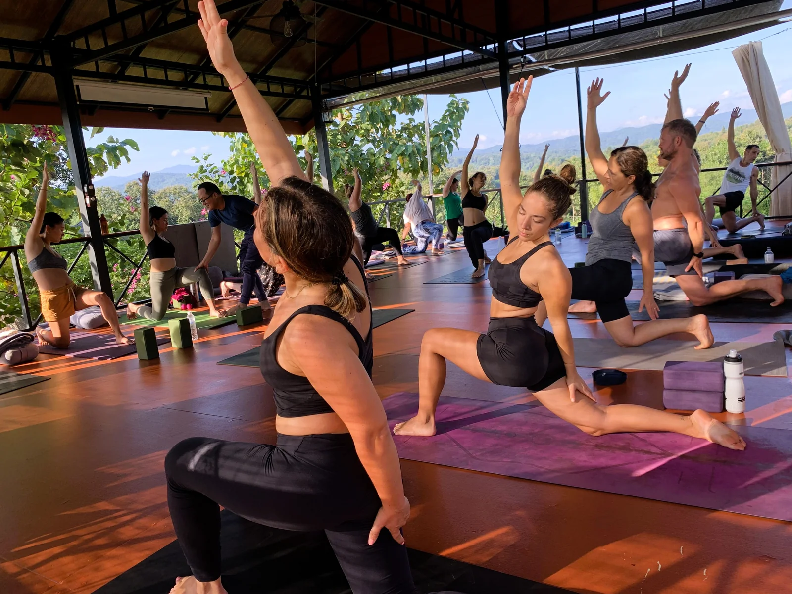 A small group practising yoga in the open-air shala with green hills beyond
