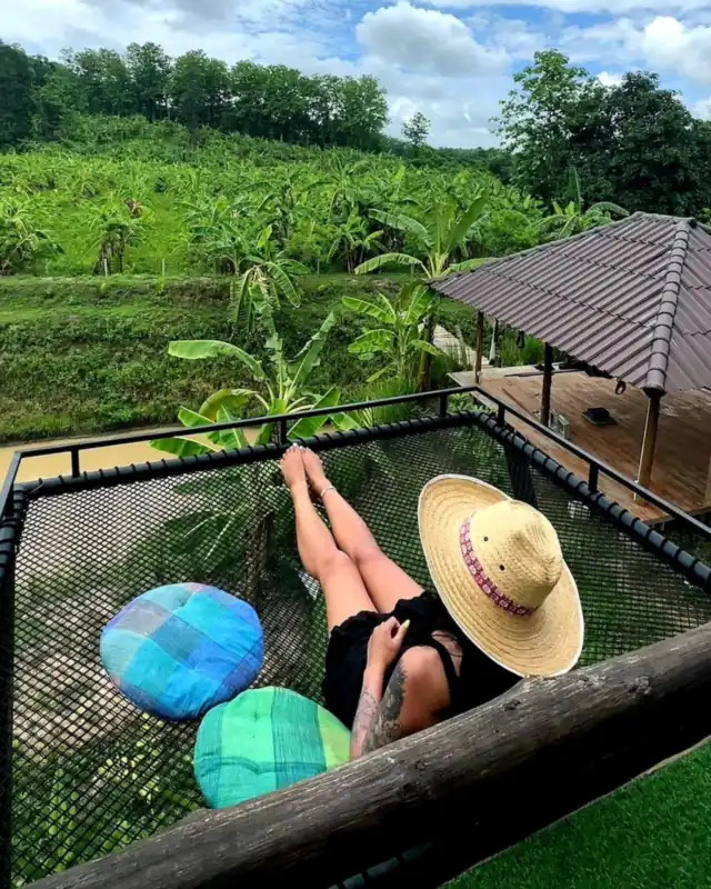 A guest in a sun hat relaxing on the Earth House balcony hammock