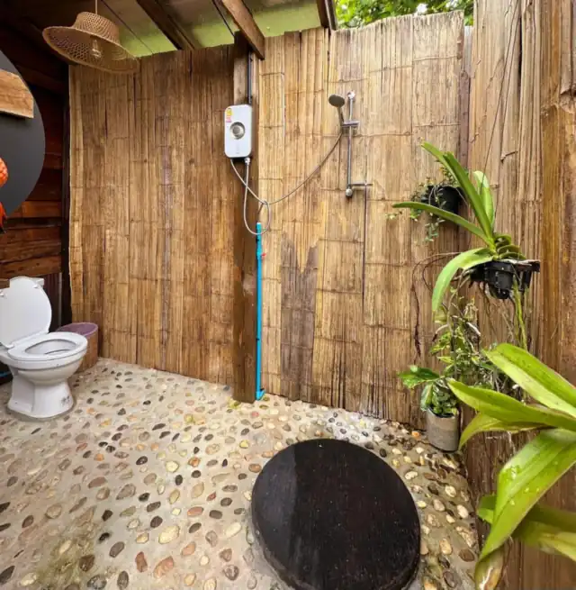 An open-air pebble-floored bathroom with bamboo walls