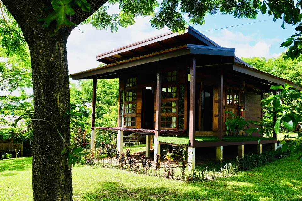 A wooden guest cottage and shaded veranda surrounded by the True Nature garden