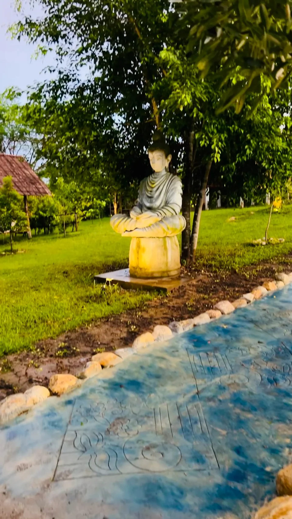 The Buddha statue beside the blue garden path and trees at True Nature