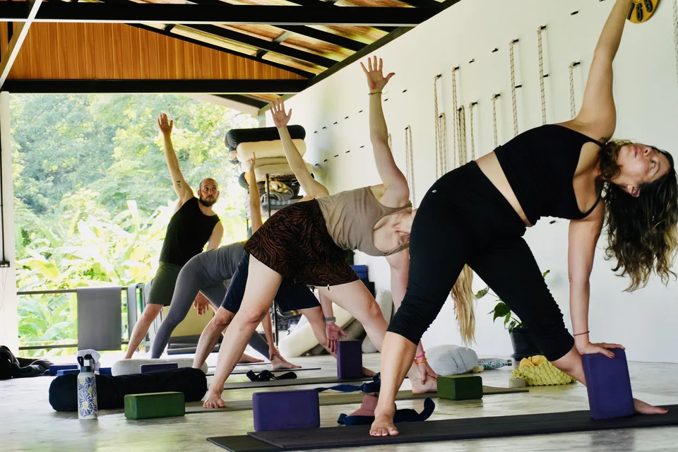 Guests practising a supported triangle pose together in the open-air True Nature shala