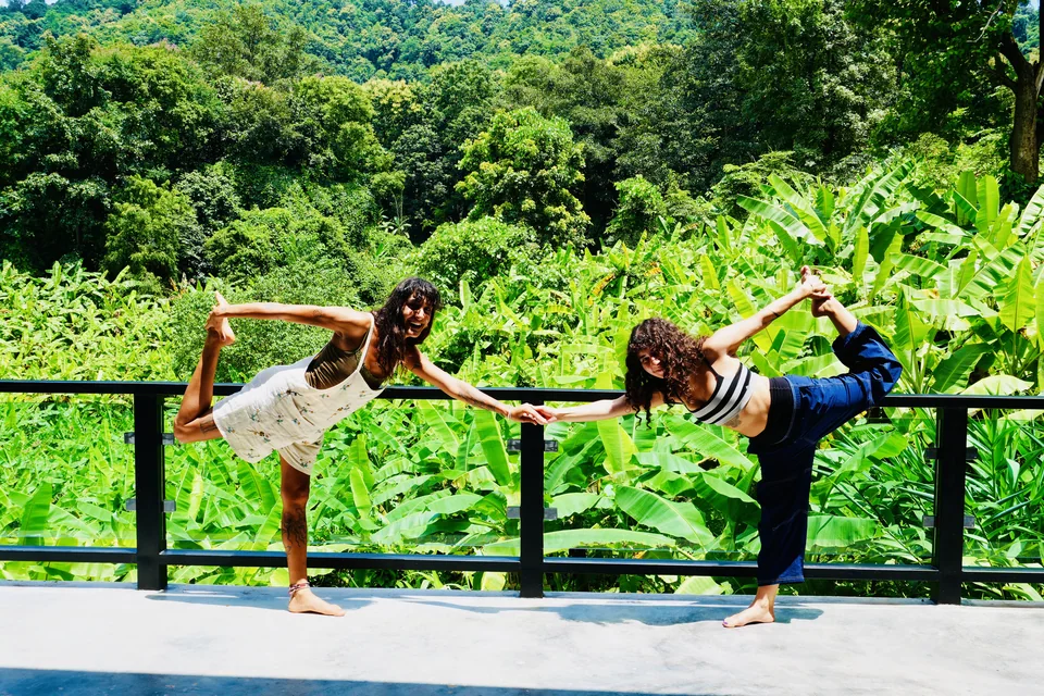 Two teacher training students practising a balancing posture together beside the banana plantation