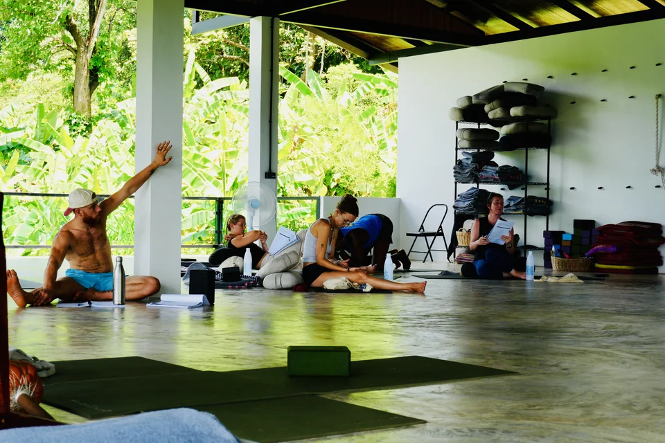 Students learning floor-based postures together in the mountain-facing shala