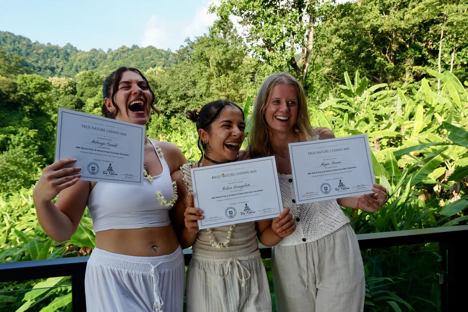 Three smiling teacher training graduates holding their certificates in the green hills